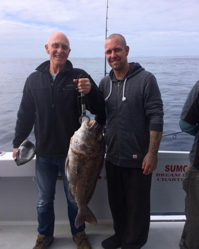 two men standing on a boat holding a fish at Moko Hiwi Escape Ruakākā- Sea View Home in Ruakaka