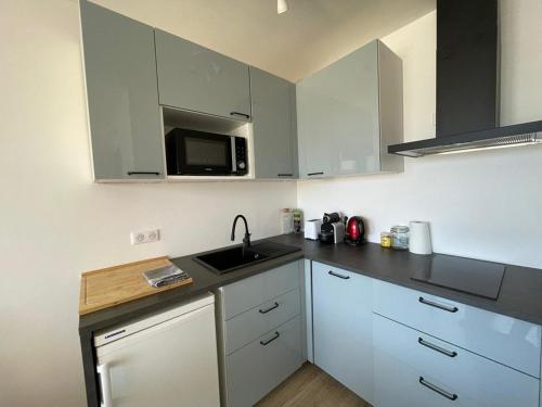 une cuisine avec des armoires blanches, un évier et un micro-ondes dans l'établissement Charmant Studio Rénové au Port de Capbreton - Idéal Pour 4 Pers. - FR-1-413-247, à Capbreton