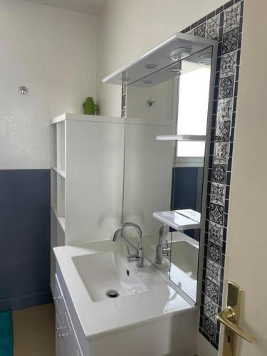 une salle de bain blanche avec un lavabo et un miroir dans l'établissement Maison proche plage, à Flamanville