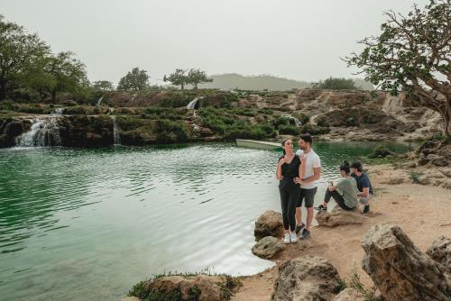 a family standing in front of a pond with a waterfall at Fanar Hotel & Residences in Salalah