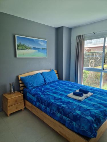 a bedroom with a bed with blue sheets and a window at Grandblue condominium 106,302 in Mae Pim