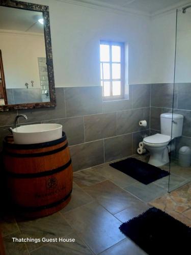 a bathroom with a sink and a toilet and a large wooden barrel at Thatchings Bed and Breakfast in Nottingham Road