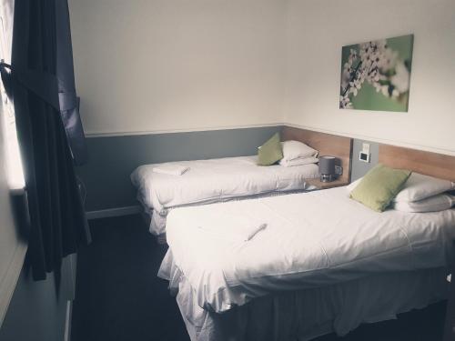 two beds in a room with white sheets and green pillows at Brewers Lodge in Blackwood