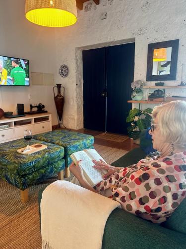 an older woman sitting on a couch reading a book at A Casa do Jaime in Prainha de Baixo