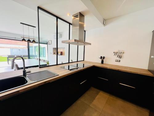 - une cuisine avec des placards noirs, un évier et des fenêtres dans l'établissement L'Escapade - Villa avec piscine, à La Rochelle