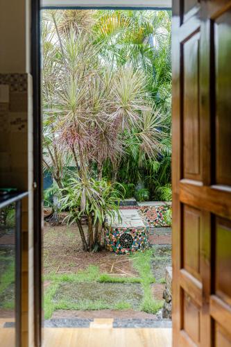 a door view of a palm tree in a yard at Mistral Holidays Near Trinity Beach & Benaulim Beach in Benaulim