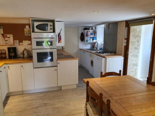une cuisine avec des armoires blanches, une table et un micro-ondes dans l'établissement La Ville Hello, A Spacious House, Sleeps 9, In Rur, à Guillac