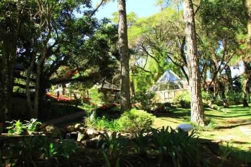 a garden with trees and a house in the background at Pousada Cantos e Contos in Monte Verde