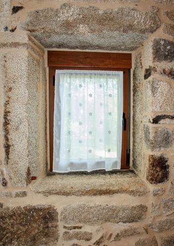 a window in a stone building with a curtain at Alojamiento Pazos in Cea