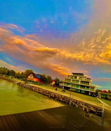 a building next to a river with a cloudy sky at Infinity Apartman Lellemarine in Balatonlelle