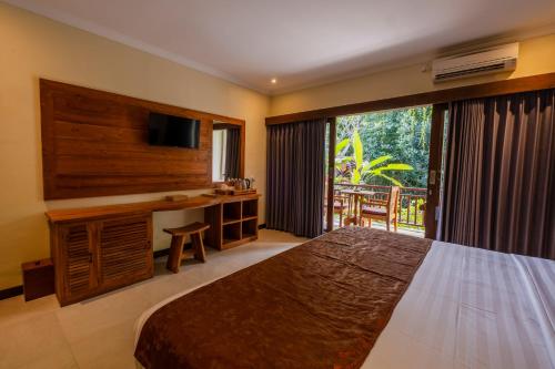 a bedroom with a bed and a desk and a window at Alamdini Resort Ubud in Ubud