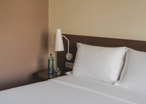 a bed with white sheets and a lamp on a table at Hotel Spa Mediterraneo Park in Roses