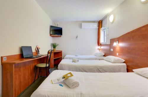 a hotel room with two beds and a desk with a laptop at Brit Hotel Reims La Pompelle in Reims