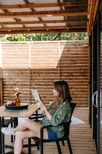 a woman sitting at a table reading a newspaper at Slow Village Anduze - Cévennes in Corbés