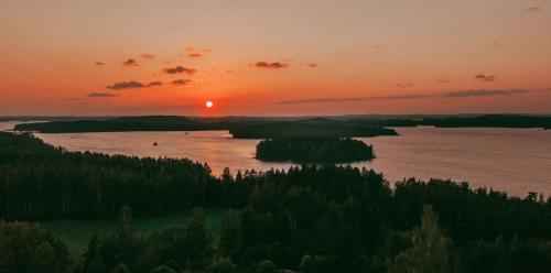 een zonsondergang boven een waterlichaam met bomen bij Metsäsydän huonemajoitus in Puumala