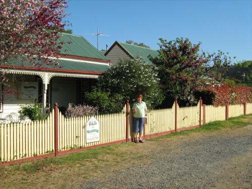 
a woman standing in front of a fence next to a house at Cuddledoon Cottages Rutherglen in Rutherglen
