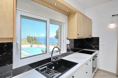 a kitchen with a sink and a window with a swimming pool at Villa Mirage Skopelos in Skopelos Town