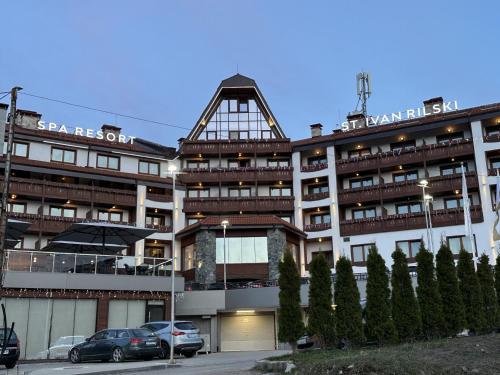 un grand bâtiment avec des voitures garées devant dans l'établissement Family Luxury Private Apartments in 4 star SPA Resort St Ivan Rilski, Bansko, à Bansko