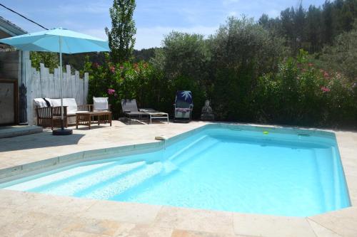 une grande piscine bleue avec une terrasse et un parasol dans l'établissement Gite l'Instant - Au cœur d'une oliveraie, à Belgentier