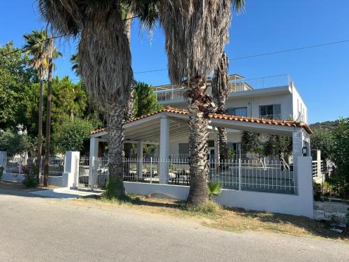 a white house with a fence and palm trees at Evia Bay Suites and Retreats in Edipsos