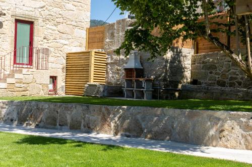 a building with a stone wall and green grass at Cruzeiros Guest House, piscina, jacuzi, grupos in Tangil