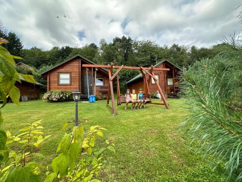 two people sitting on a swing in front of a cabin at Bieszczady Pod Dębem Solina in Solina