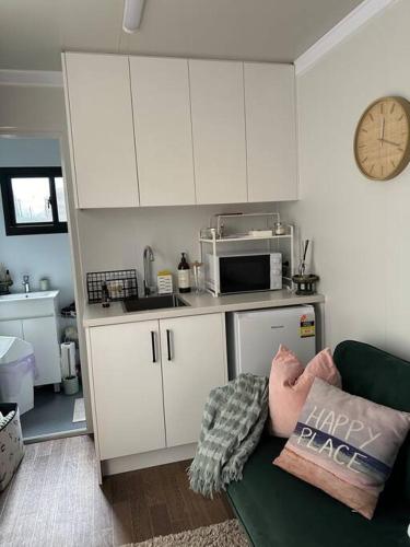 a kitchen with white cabinets and a green couch at Tiny Home Beach Serenity! in Sydney
