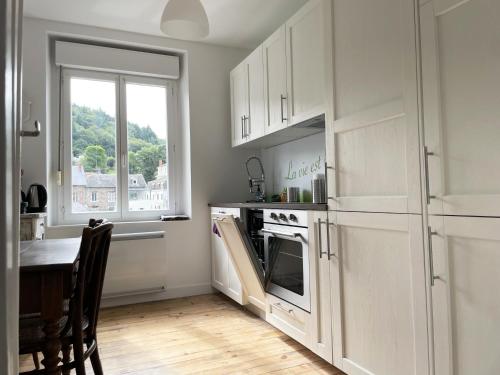 une cuisine avec des armoires blanches, une table et une fenêtre dans l'établissement Appartement Louison jusqu'à 4 personnes, à Bort-les-Orgues