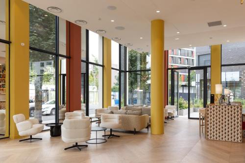 a lobby with chairs and tables and windows at Hôtel Kyriad Prestige Paris Asnieres in Asnières-sur-Seine