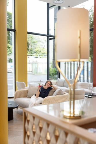 a woman laying on a couch in a living room at Hôtel Kyriad Prestige Paris Asnieres in Asnières-sur-Seine