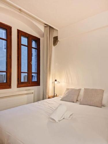 un lit blanc dans une chambre avec deux fenêtres dans l'établissement Manaslu plein centre charmant et chaleureux, à Annecy