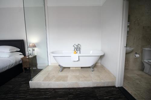a white bath tub in a bedroom with a bed at The Saracens Head Hotel - The Coaching Inn Group in Great Dunmow