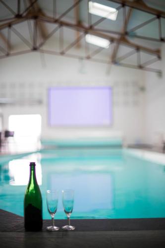 two wine glasses and a bottle on a table next to a swimming pool at Villa moderne proche du Mans avec piscine intérieure in Dollon