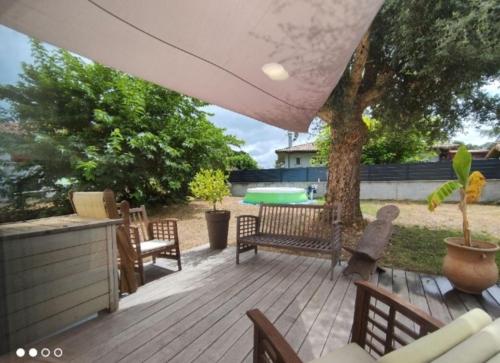 eine Terrasse mit Tisch und Stühlen und einem Baum in der Unterkunft Maison climatisee 8 couchages avec piscine a Mimizan Plage notée superhote in Mimizan