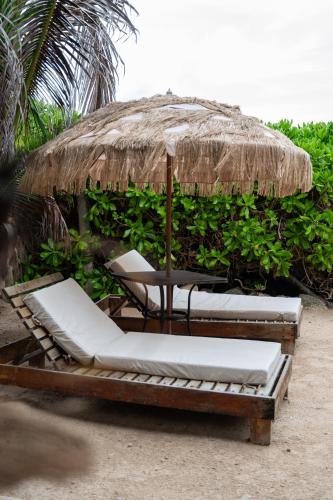 two lounge chairs and an umbrella on a beach at Tropicalito Villa on the Beach in Tulum