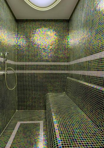 a green tiled bathroom with a shower with a bench at Gleam Bomonti Hotel in Istanbul