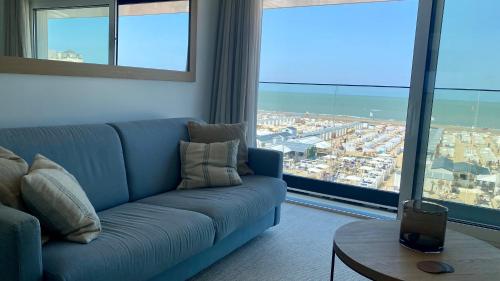 a living room with a blue couch and large windows at Royal Knokke in Knokke-Heist
