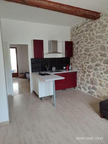 - une cuisine avec des placards rouges et un mur en pierre dans l'établissement La Porte Verte, à Capendu