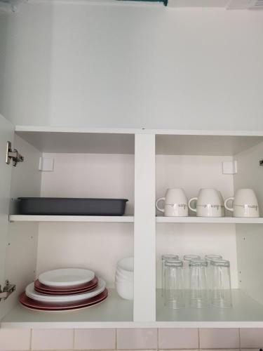 une cuisine blanche avec des assiettes, des tasses et des plats dans l'établissement Soleil, à Itteville