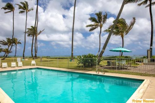 a swimming pool with palm trees and an umbrella at NEW Beachfront Condo in Hauula