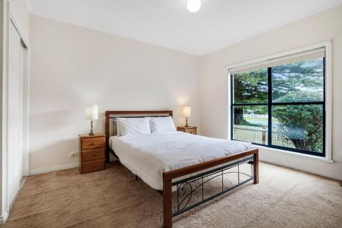 a white bedroom with a bed and a large window at Kurrawa in Port Fairy