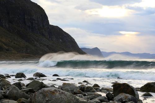 a wave crashing on a rocky beach next to a mountain at Alnes Gård in Ålesund