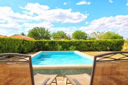 a swimming pool with two chairs next to a hedge at Casa Brisa, Gran Pacifica in Managua