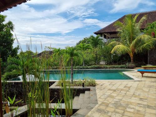a swimming pool with palm trees and a house at Villa Ponjok Batu Residence in Bukti