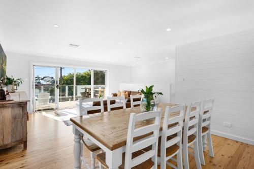a white dining room with a wooden table and chairs at "Casa di Mare=" House by the Sea - Belle Escapes Jervis Bay in Vincentia
