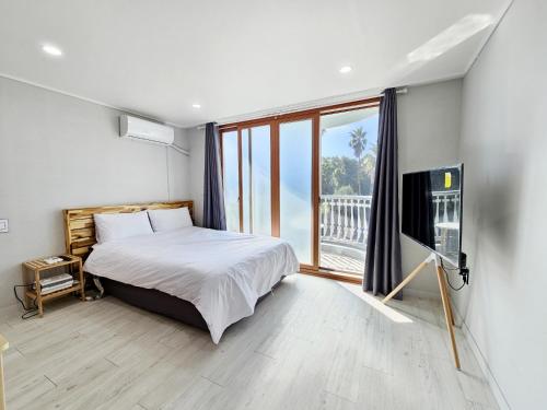 a bedroom with a bed and a large window at Greenside Pension in Seogwipo