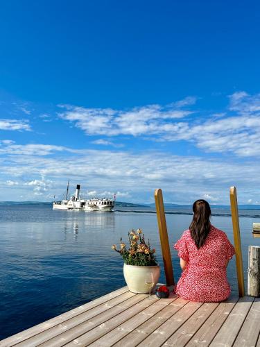 a woman sitting on a dock looking at a boat in the water at Idylliske Evjua ved Mjøsa in Skreia