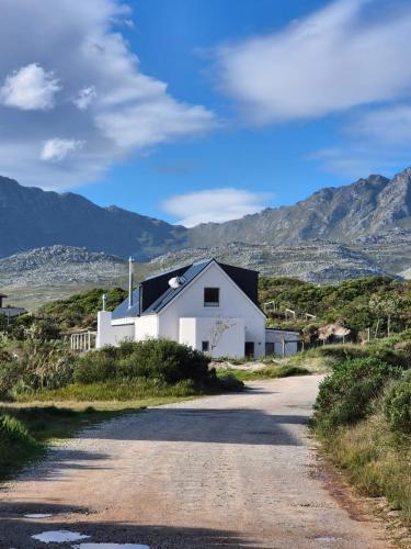 a white house on a road with mountains in the background at The Dunes Pringle Bay in Pringle Bay