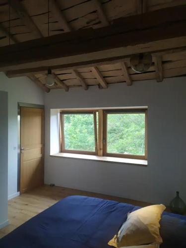 une chambre avec un lit bleu et deux fenêtres dans l'établissement Gîte avec jardin, à Légny