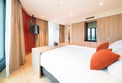 a bedroom with a large white bed with orange pillows at Hotel du Bois d'Arlon in Arlon